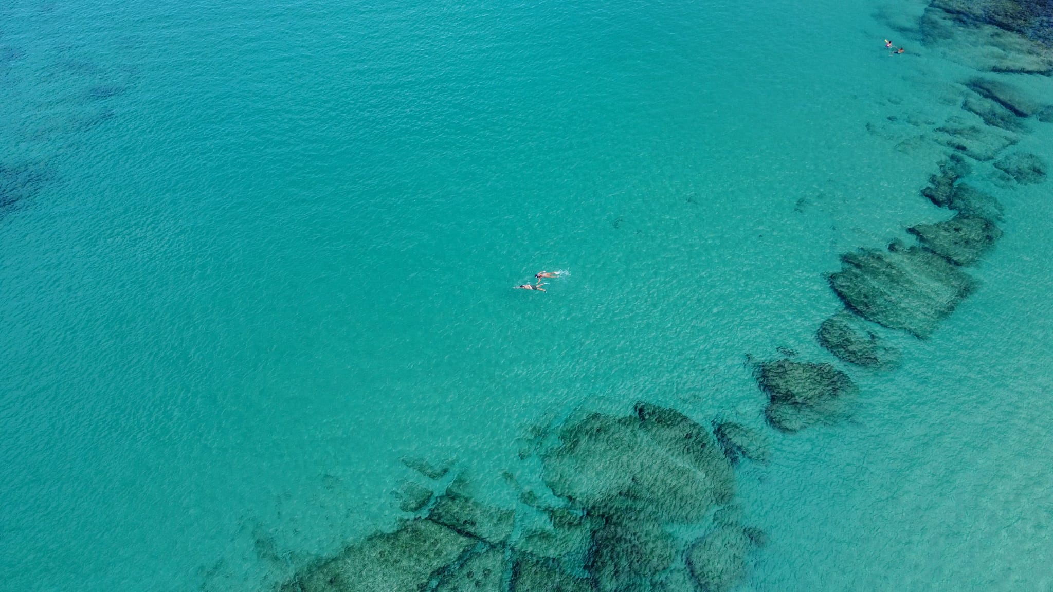 DJI_0919 Napili Village Hotel, Aerial view of turquoise water with swimmers and underwater rock formations. About Us.