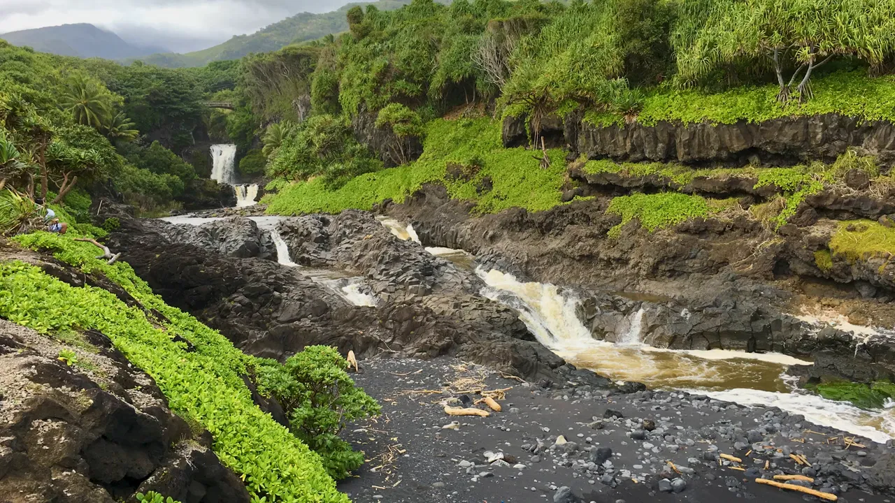 The Pools of ʻOheʻo with multiple cascading waterfalls, black sand beach and green cliffs