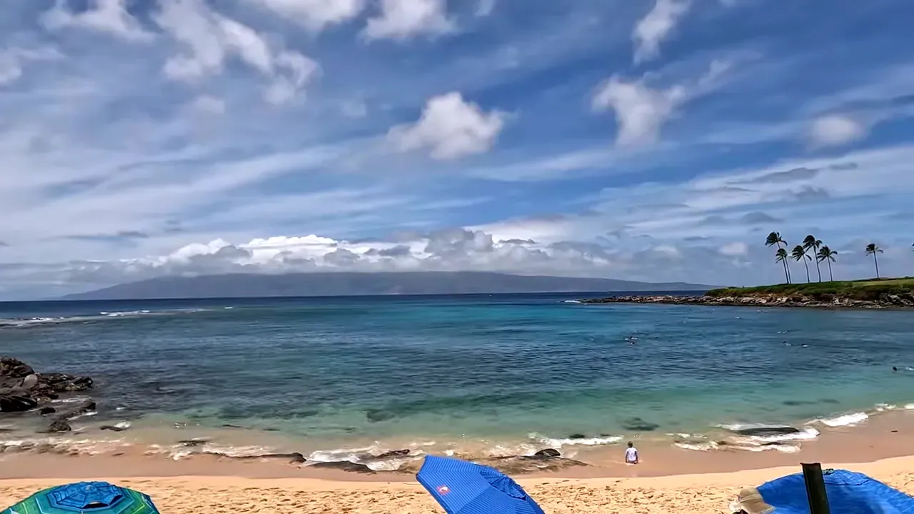 Wide view of Kapalua Bay showing sandy beach, swimmers and a distant island on the horizon